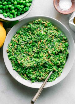 green pea pesto in a white bowl with a gold fork on a white table