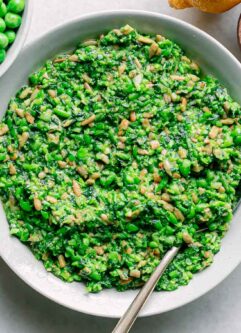 a bowl of green pea pesto on a white table with a bowl of fresh spring peas