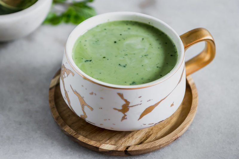 a mug of matcha green tea latte with a mint leaf and a sprinkle of green tea powder on top