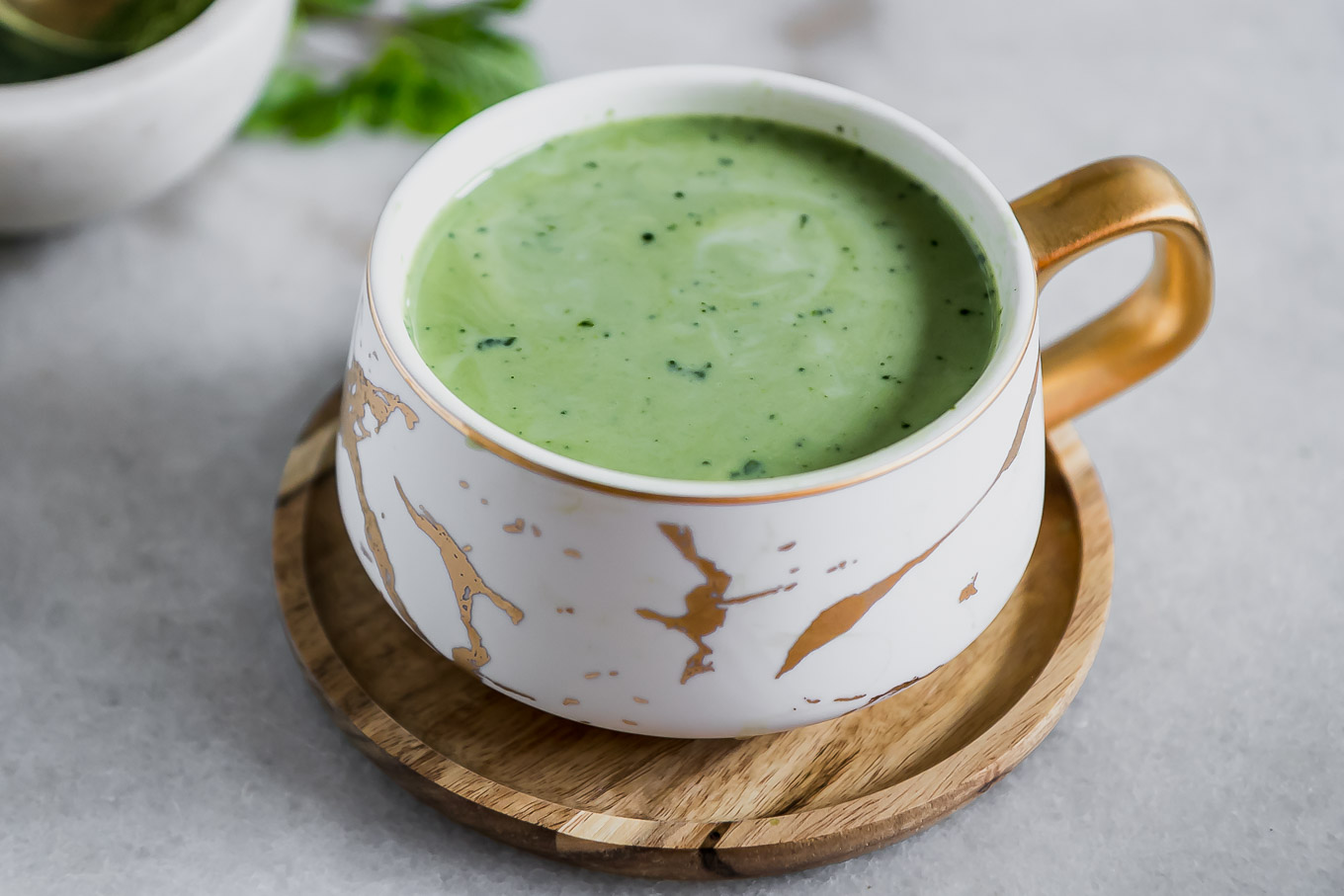 a mug of matcha green tea latte with a mint leaf and a sprinkle of green tea powder on top