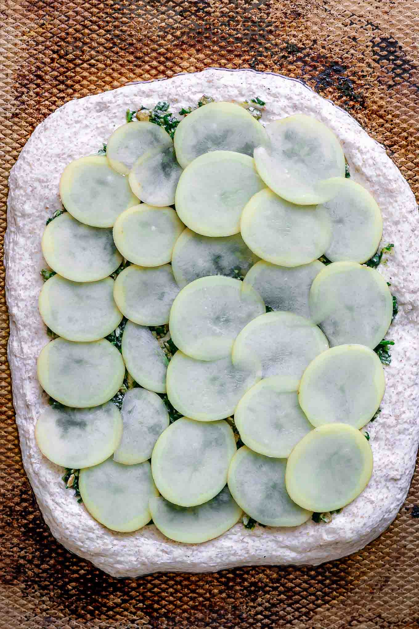 sliced potatoes on pizza dough on a baking sheet