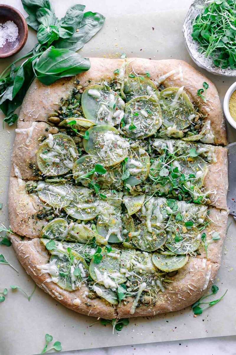 plant-based pesto pizza with potatoes on a white table with fresh basil leaves