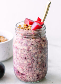 purple plum overnight oats in a jar with granola and cut plums as garnish on a white table