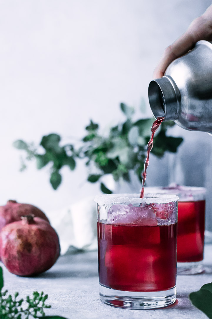 a hand pouring a pomegranate margarita into a glass with a salt and sugar rim
