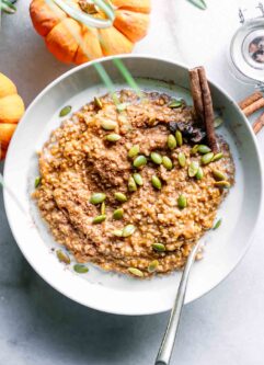 a bowl of oatmeal with pumpkin and pumpkin seeds on a white table with mini pumpkins