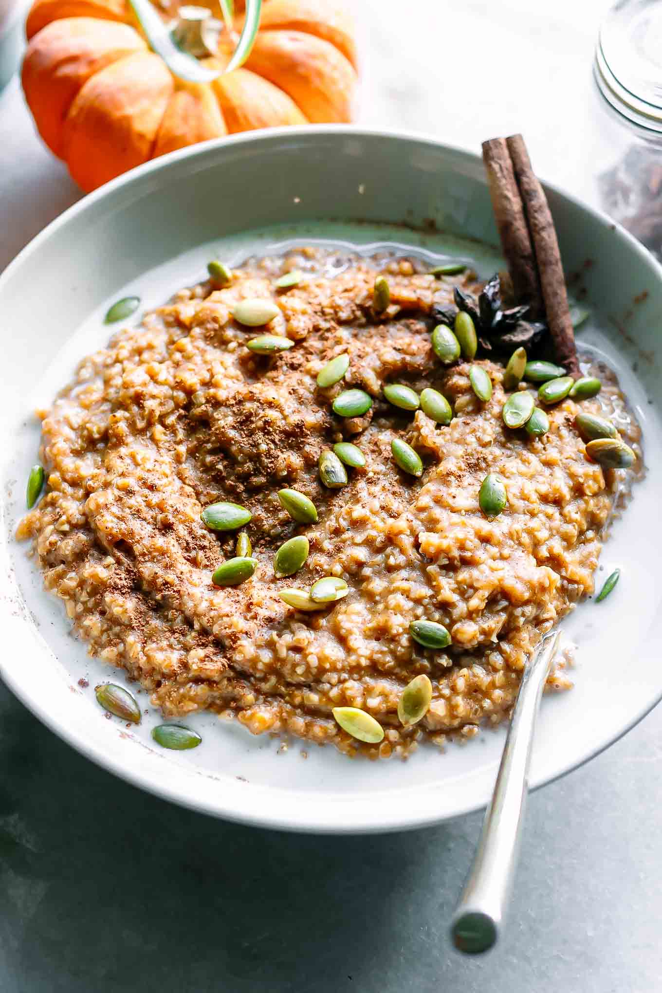 a white bowl of oatmeal with pumpkin with a gold fork on a white table