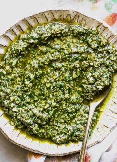pumpkin seed pesto on a white plate on a white table with bowls of pumpkin seeds and salt