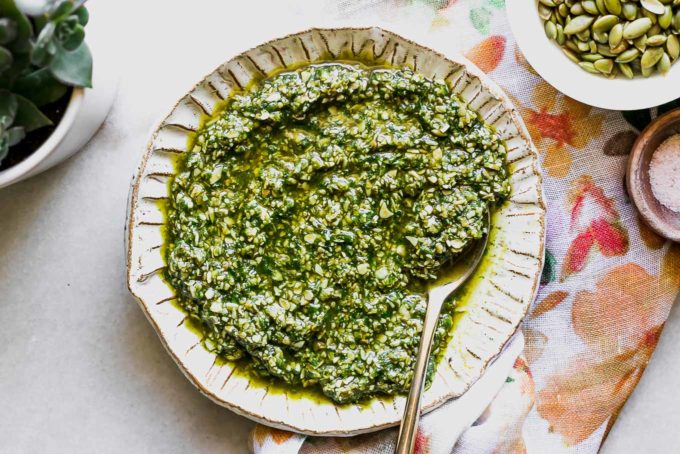 pumpkin seed pesto on a white plate on a white table with bowls of pumpkin seeds and salt