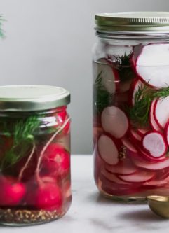 two jars of sliced and whole pickled radishes on a white table