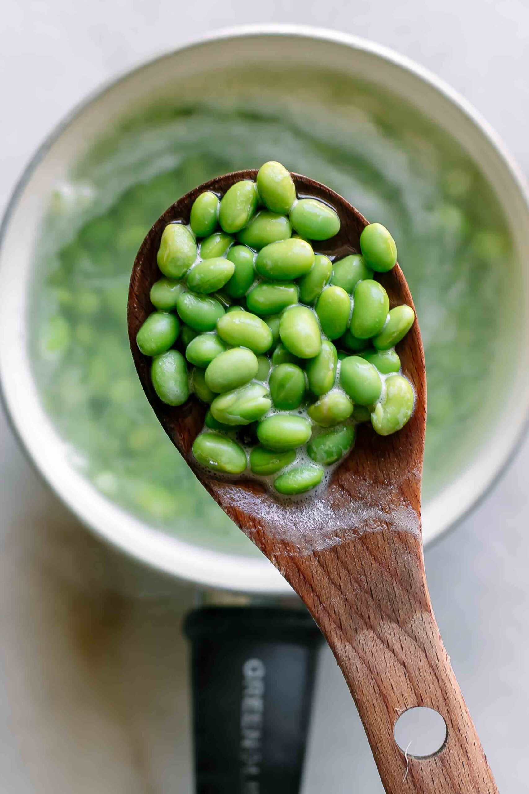 cooked edamame on a wooden spoon over a small pot of hot water