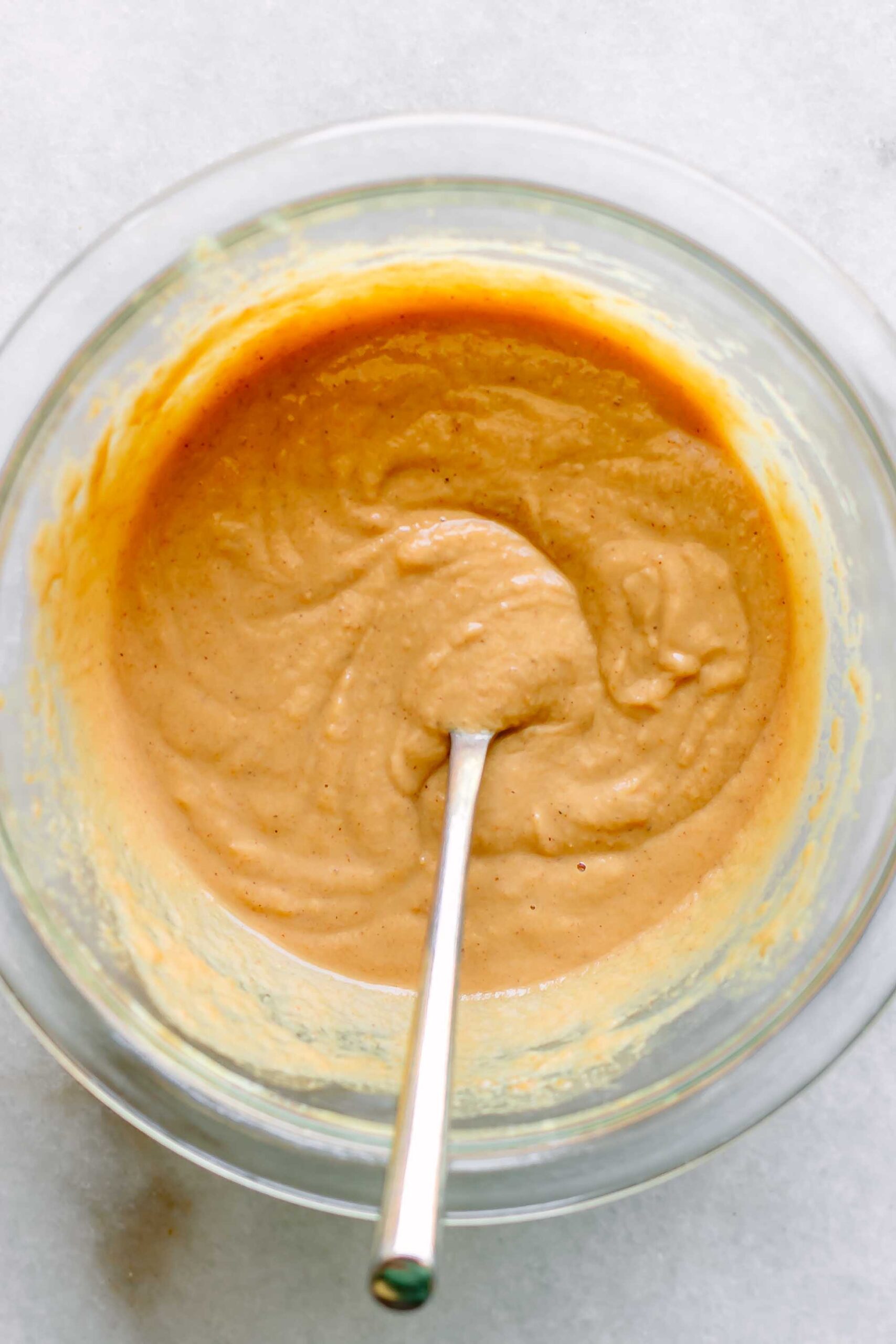 a bowl of peanut sauce with a gold spoon on a white table