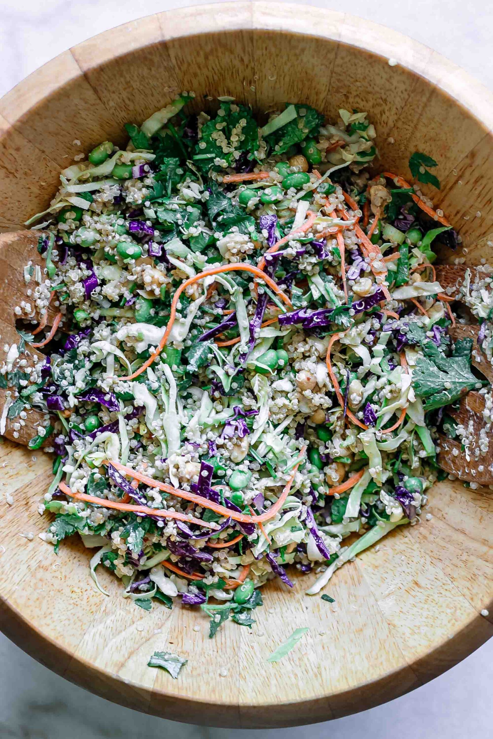 a large wooden bowl with a cabbage, carrot, and quinoa salad on a white table