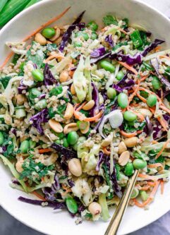 a white bowl with a cabbage and quinoa salad with a gold fork on a white table