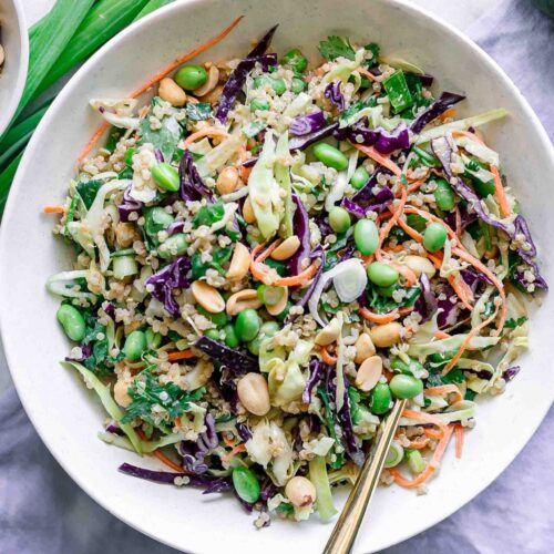a white bowl with a cabbage and quinoa salad with a gold fork on a white table