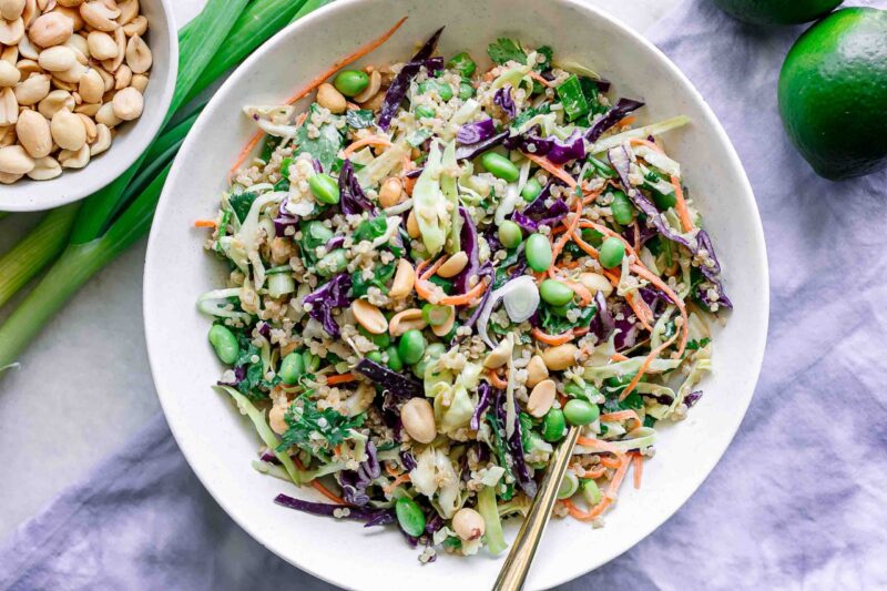 a white bowl with a cabbage and quinoa salad with a gold fork on a white table