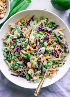 a white bowl with a cabbage and quinoa salad with a gold fork on a white table