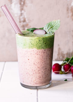 a radish and radish greens layered smoothie in a glass with a straw on a white table with fresh radishes