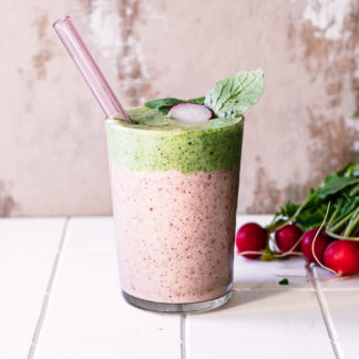 a radish and radish greens layered smoothie in a glass with a straw on a white table with fresh radishes