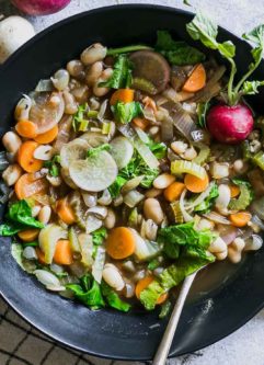 vegetable soup with radishes and radish greens in a bowl on a table with a gold fork
