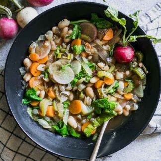 vegetable soup with radishes and radish greens in a bowl on a table with a gold fork