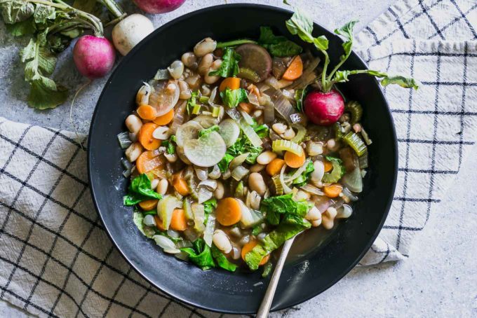 vegetable soup with radishes and radish greens in a bowl on a table with a gold fork