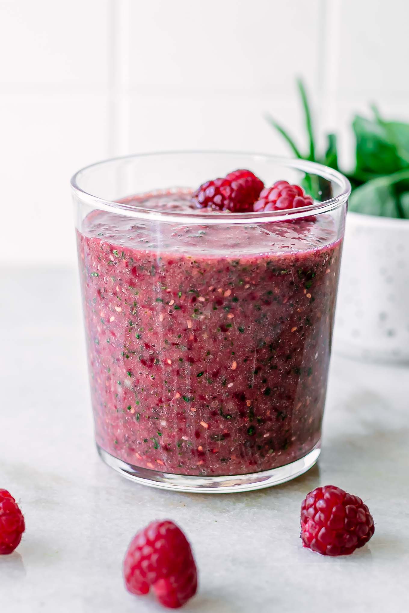 a glass with a red and green raspberry and spinach smoothie on a white countertop