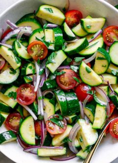 a raw zucchini tomato onion and basil salad in a white bowl on a white table with fresh basil