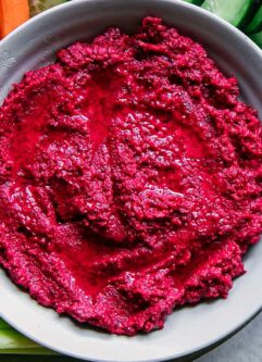 a bowl of red beet hummus on a plate with vegetable