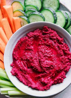red beet hummus in a bowl with cut vegetables for dipping on a blue plate