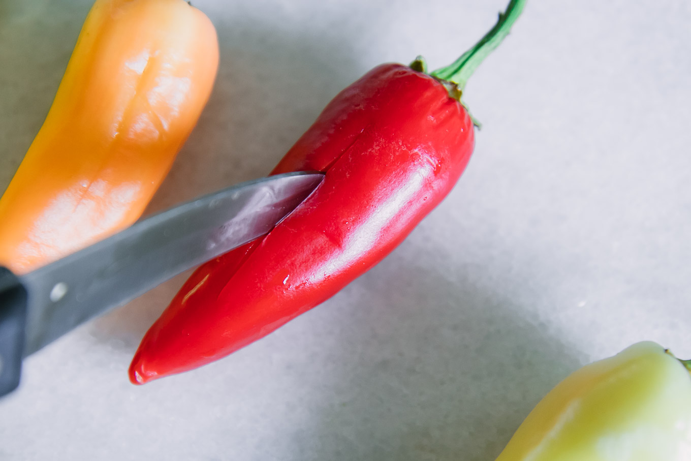 a knife cutting a slit into a red pepper