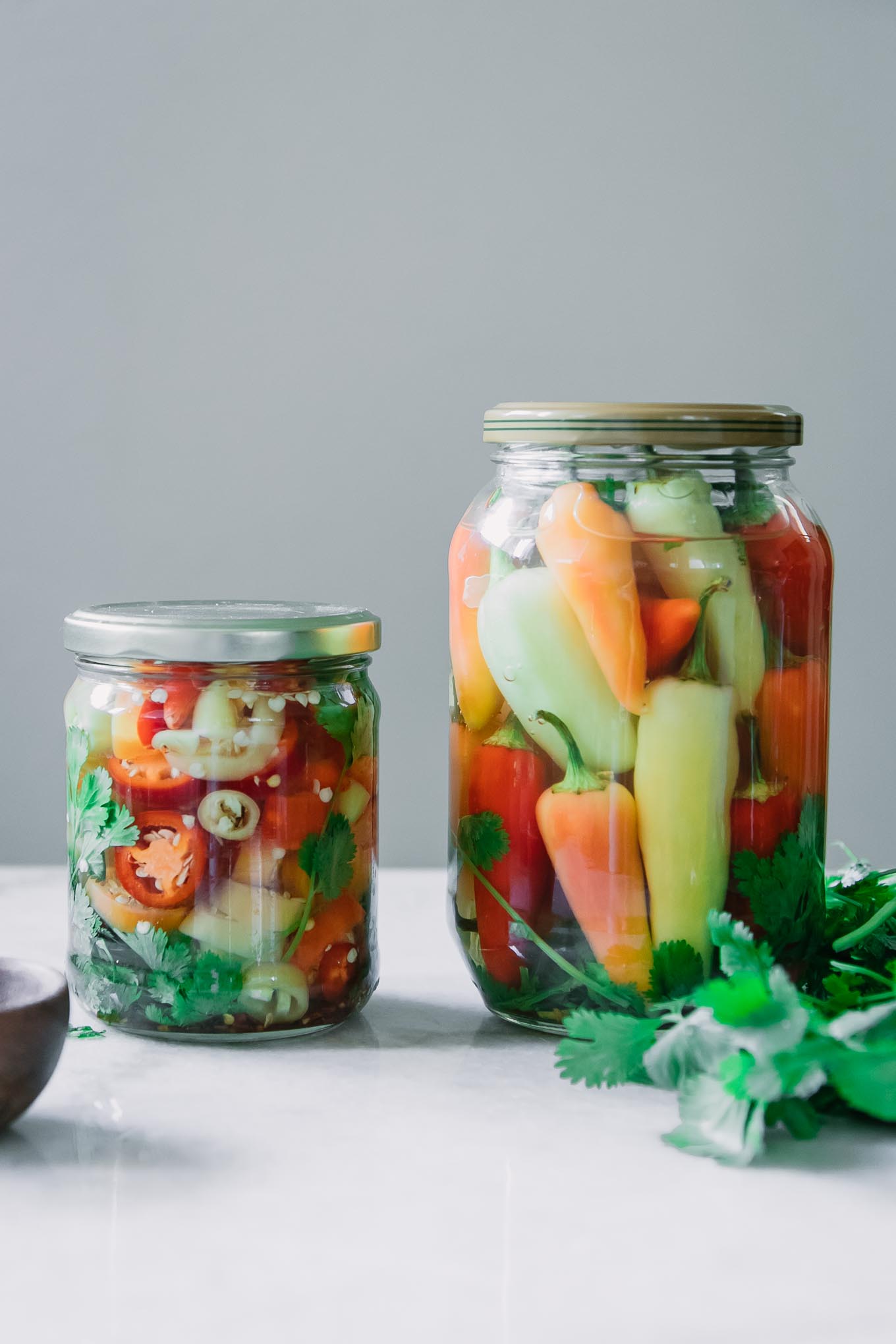 two jars of pickled peppers, one with sliced peppers and one with whole peppers