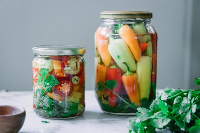 two jars of pickled peppers on a white table with fresh cilantro