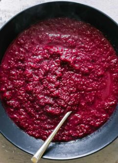 a bowl of red beet apple soup on a wood table with a gold fork