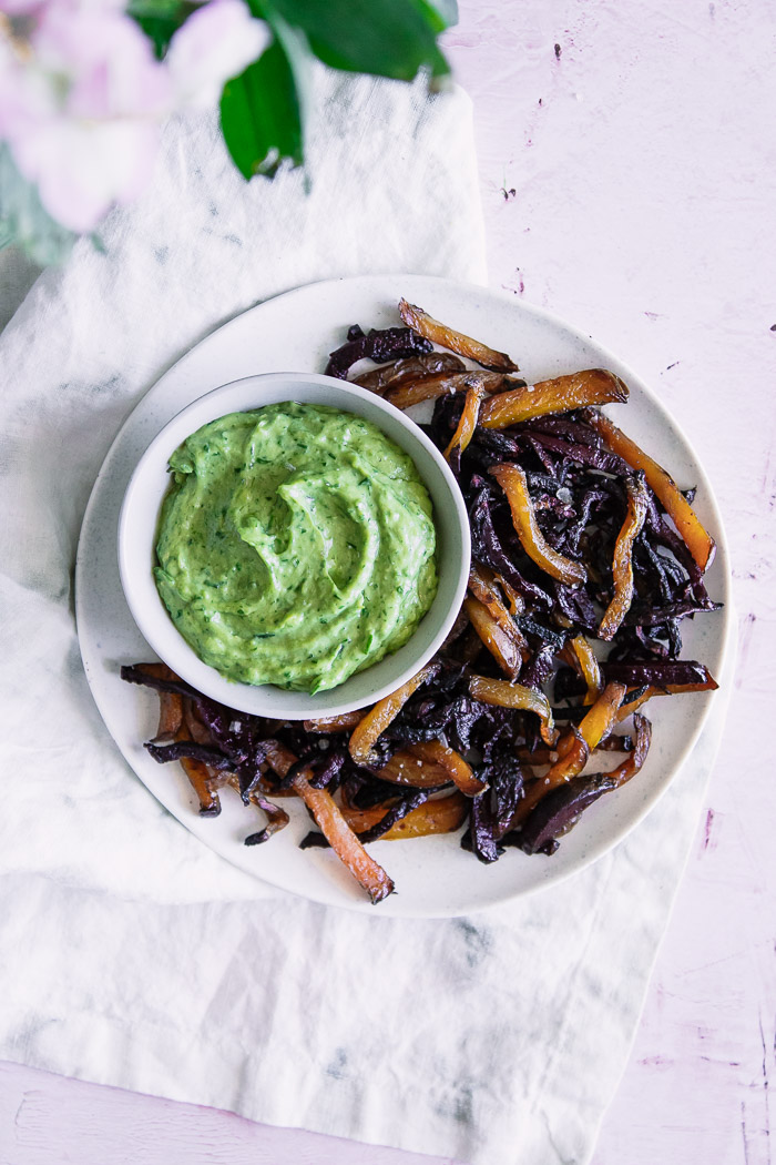 Roasted beets on a white plate with green dip on a pink table.