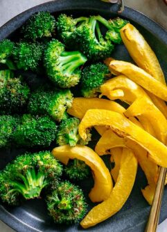 roasted broccoli and acorn squash on a blue dish on a white table with a gold fork