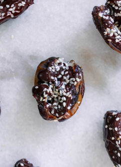 tahini stuffed dates coated with chocolate and sprinkled with sesame seeds on a white table