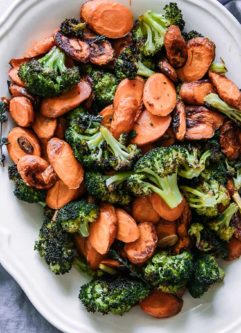 roasted carrots and broccoli on a white plate with a blue napkin and a small bowl of salt