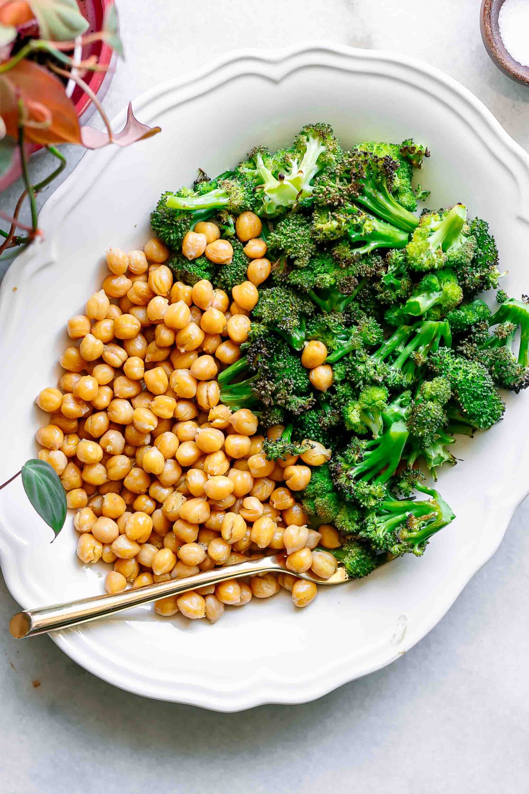 a white plate with roasted chickpeas and broccoli on a white table