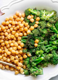 a white plate with roasted broccoli and chickpeas on a white table with a gold fork