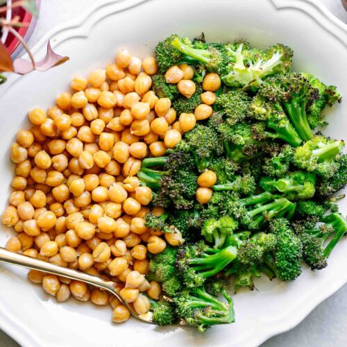 a white plate with roasted broccoli and chickpeas on a white table with a gold fork