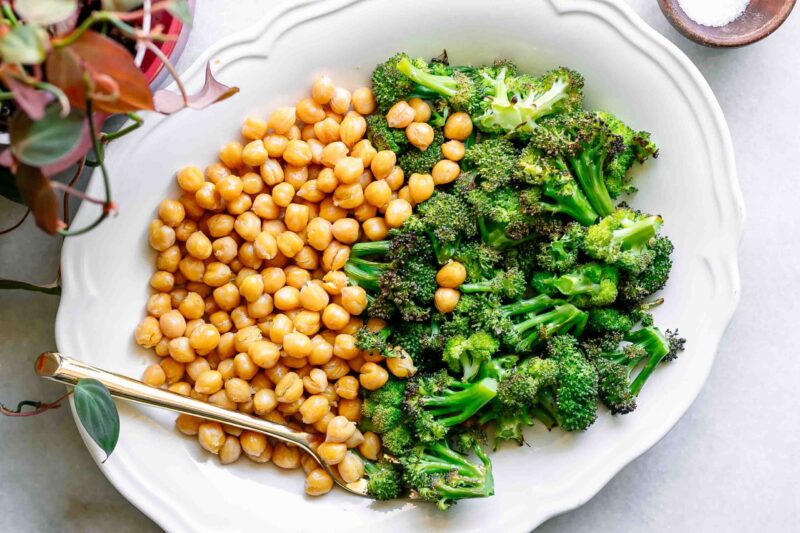 a white plate with roasted broccoli and chickpeas on a white table with a gold fork