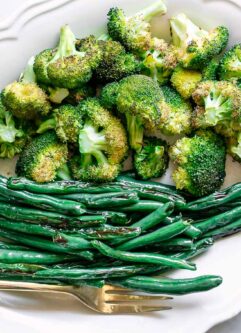 roasted broccoli and green beans on a white side dish with a gold fork on a white table