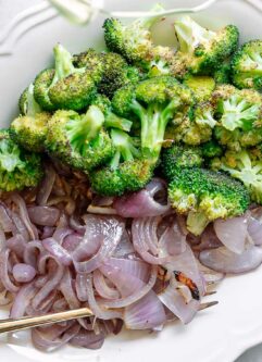 roasted broccoli and onions on a white side dish with a gold fork on a white table