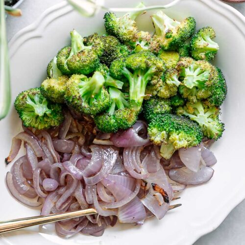 roasted broccoli and onions on a white side dish with a gold fork on a white table