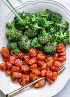 a white plate with roasted broccoli and tomatoes and a gold fork
