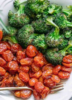 a white plate with roasted broccoli and tomatoes with a gold fork
