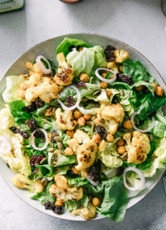 a simple greens salad with cauliflower and chickpeas on a white plate on a table with a blue napkin