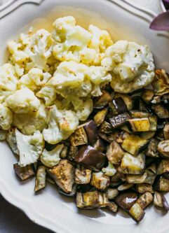 a white side dish with baked cauliflower and eggplant on a white table