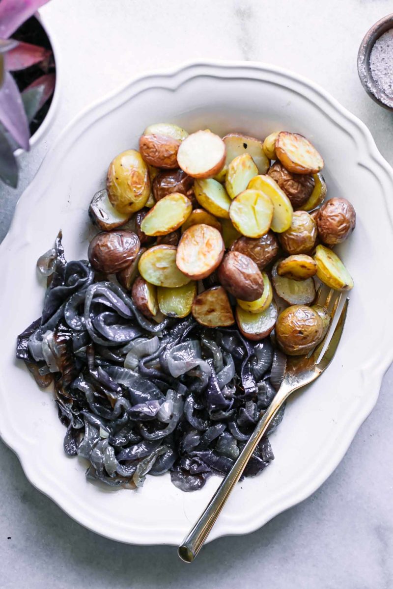 roasted onions and potatoes on a white plate with a gold fork