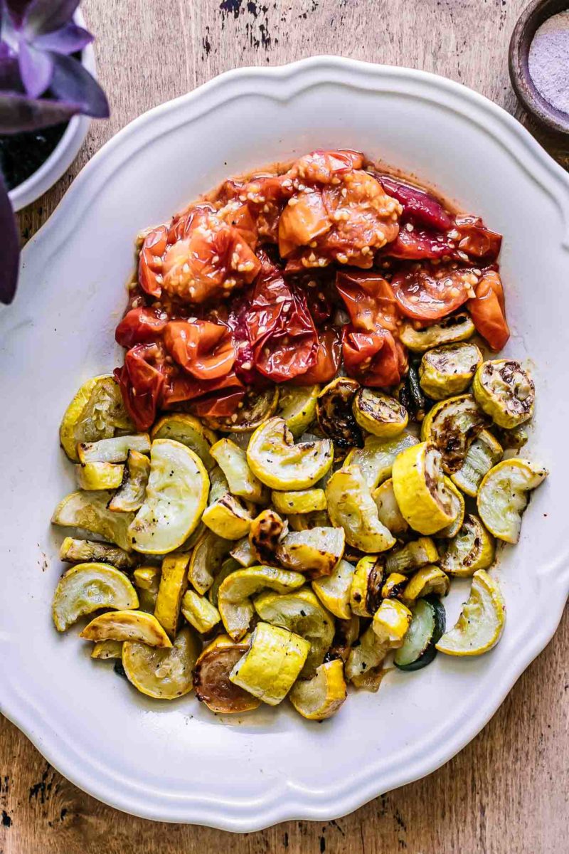 roasted summer squash and tomatoes on a white plate on a wood table